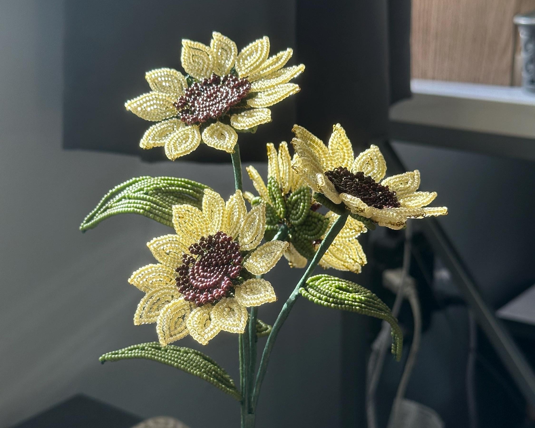 Decorative beaded sunflower arrangement in a clear vase on a desk.
